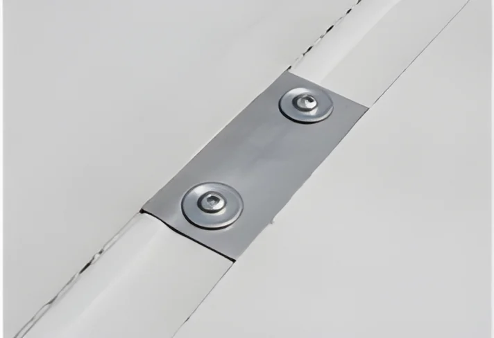 Two screws and round plates holding a white single-ply membrane along a seam before the next sheet is welded over